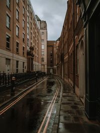 Wet street amidst buildings against sky during rainy season