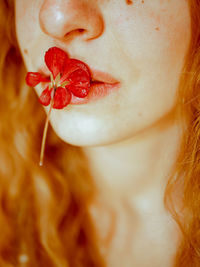 High angle view of young woman holding a red flower with her lips. blond hair, red head. 