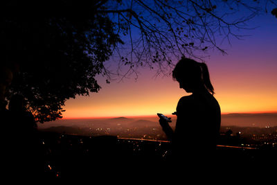 Silhouette woman using smart phone against sky during sunset