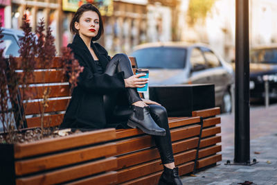 Portrait of young woman standing on railing in city