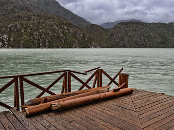Wooden railing by lake against sky