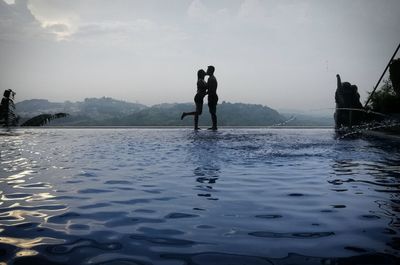Silhouette couple kissing by infinity pool against sky during sunset