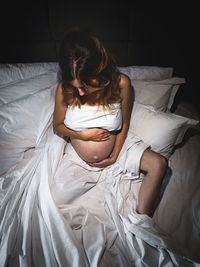 High angle view of pregnant woman sitting on bed at home