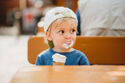 Young blonde boy with dirty face eating ice cream with a cap on