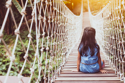 Rear view of girl sitting on footbridge