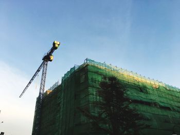 Low angle view of crane by building against clear blue sky