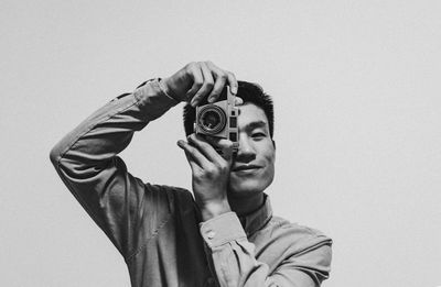Portrait of young man photographing from camera against gray background