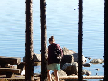 Rear view of woman standing on wooden post by sea