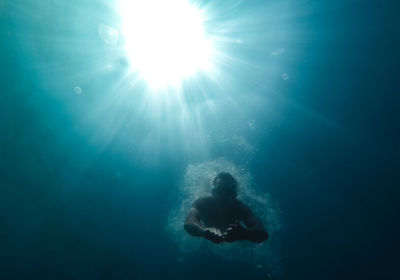 Silhouette of a man in the rays of the sun floats in the black sea