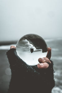 Close-up of hand holding sphere with upside down reflection of sea