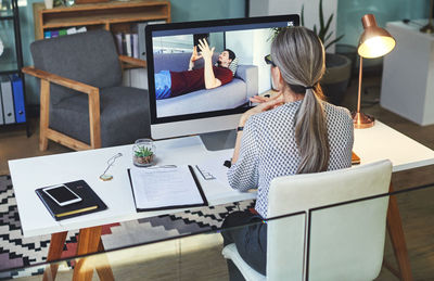 Rear view of woman using digital tablet while sitting on table