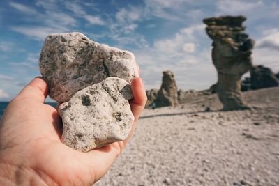 Close-up of person holding rock against sky