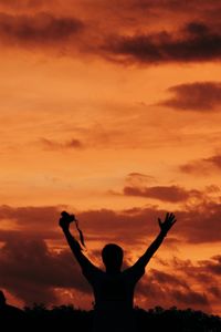 Rear view of silhouette man standing against orange sky