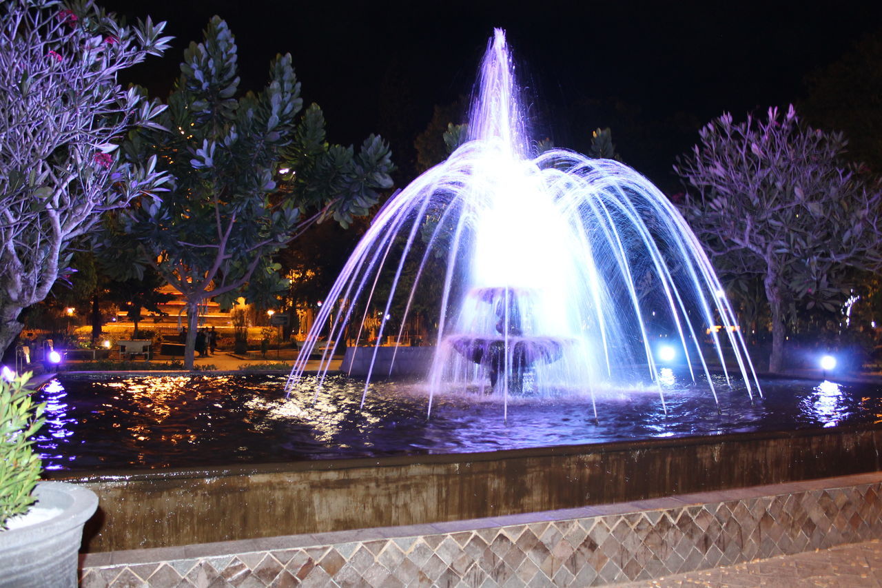 night, illuminated, long exposure, fountain, motion, built structure, architecture, building exterior, water, spraying, glowing, arts culture and entertainment, light trail, reflection, blurred motion, city, lighting equipment, travel destinations, tree, sky