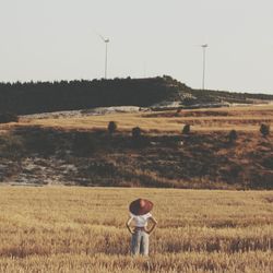 Woman standing in field of wheat and looking at hill with wind turbines