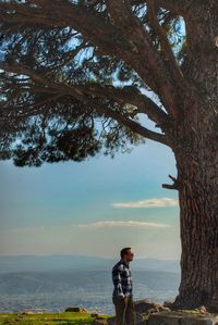 Man standing by tree trunk against sky