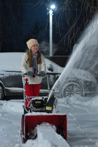 A girl in the evening in the winter at the site near the house, removes snow with a snowplow. 