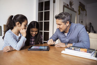 Father and daughters using looking at tablet computer while sitting by table