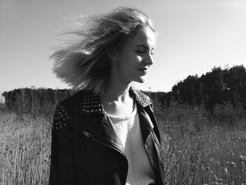 Young woman looking away while standing on field against sky