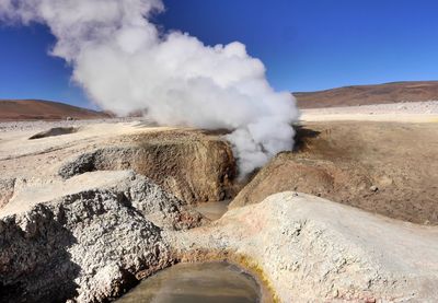 Smoke emitting from volcanic landscape against sky