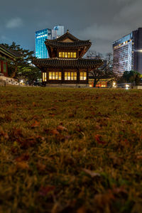 Illuminated building by field against sky at night