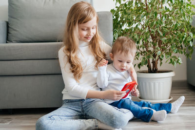 Girl with a baby brother sitting on the floor with a smartphone