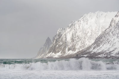 Scenic view of sea by snowcapped mountain against sky