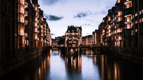 Reflection of illuminated buildings in canal against sky