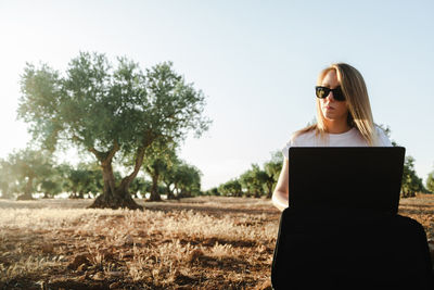 Woman using laptop while sitting at olive orchard