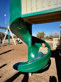 Portrait of happy boy sitting on slide at playground