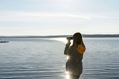 Young woman looking through binoculars at birds on lake birdwatching, ecology nature research 