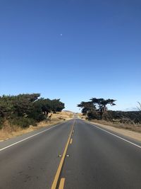 Empty road along trees against clear sky