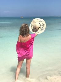 Rear view of woman holding hat while standing on shore at beach