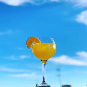 Low angle view of yellow cocktail glass against blue sky