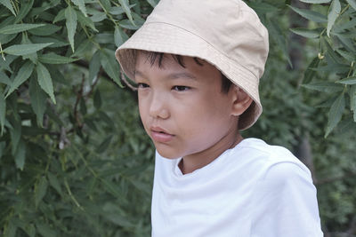 Close-up portrait of an asian boy in a white t-shirt and a panama hat on a background of nature.