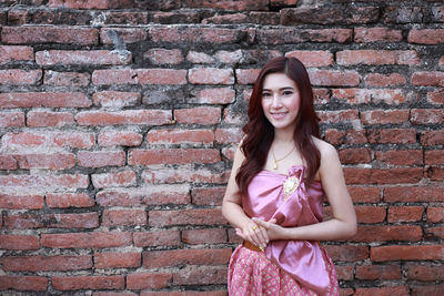 Portrait of smiling young woman standing against brick wall