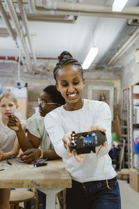 Happy female student looking at electric component in school workshop