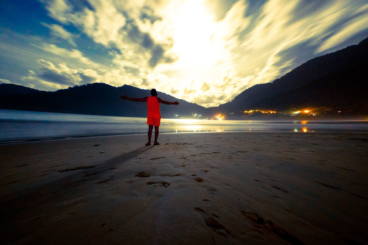 REAR VIEW OF YOUNG WOMAN STANDING ON BEACH AGAINST SKY