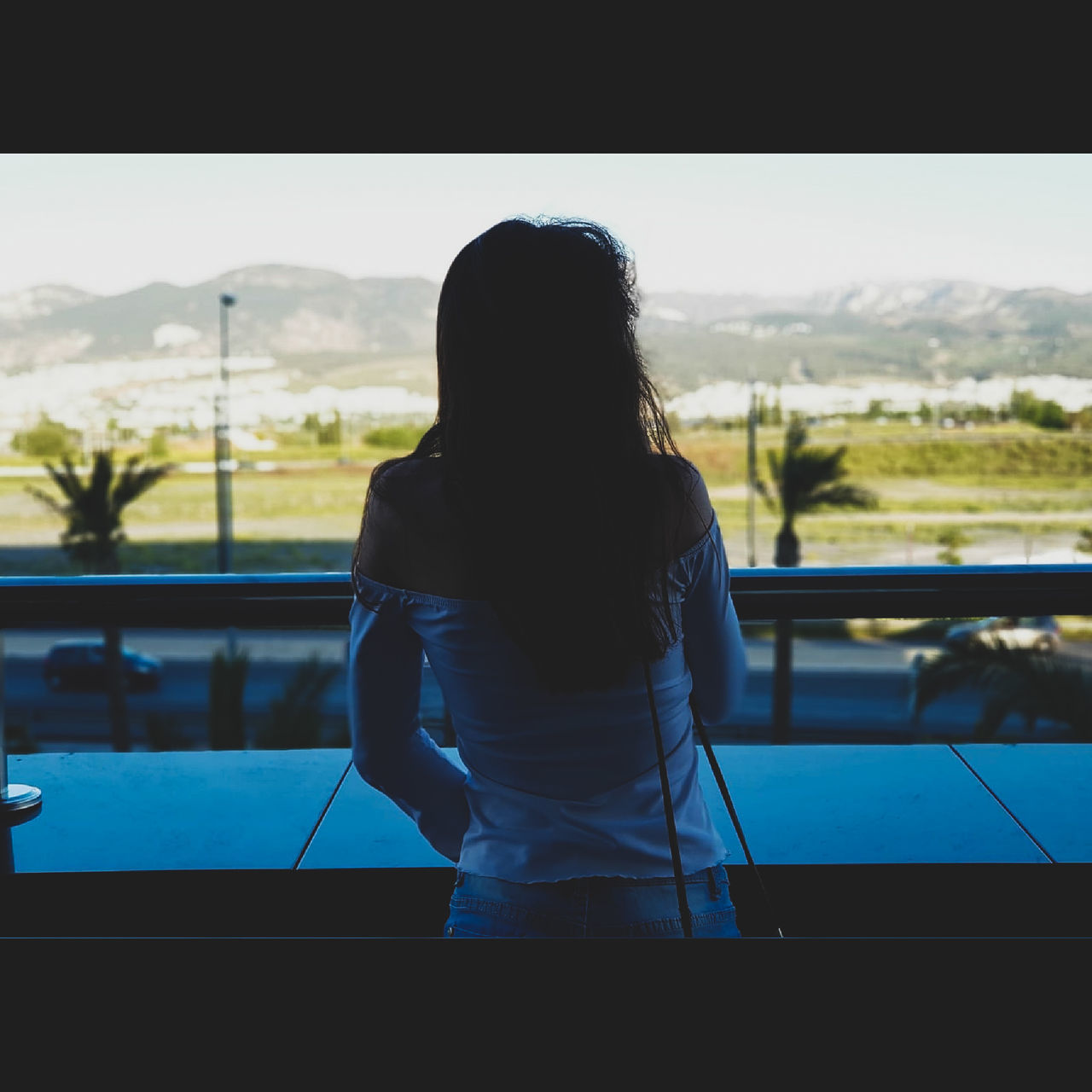 REAR VIEW OF WOMAN STANDING BY WINDOW