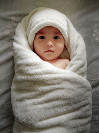 Portrait of cute baby boy wrapped in towel on bed