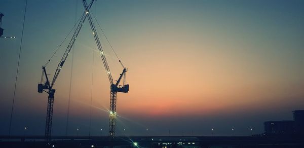 Cranes against clear sky at construction site during sunset