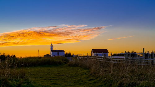 Buildings on field against sky during sunset