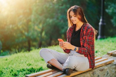 Young woman using mobile phone while sitting on camera