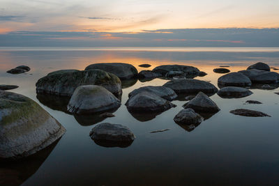 Rocks on sea shore against sky during sunset