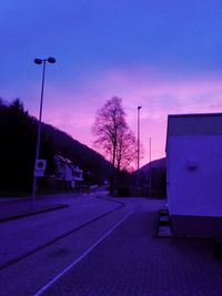 Empty road by buildings against sky at sunset