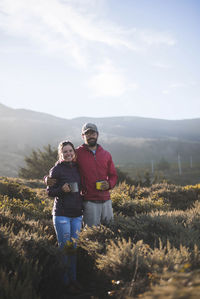 Portrait of young couple holding mugs while standing on field against sky at yosemite national park