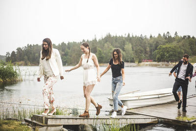 Multi-ethnic friends walking on jetty over lake during weekend getaway