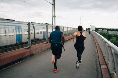 Rear view of male and female athletes running on footbridge in city