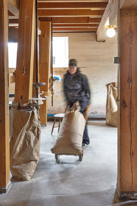 Woman in mill pushing sack on sack barrel