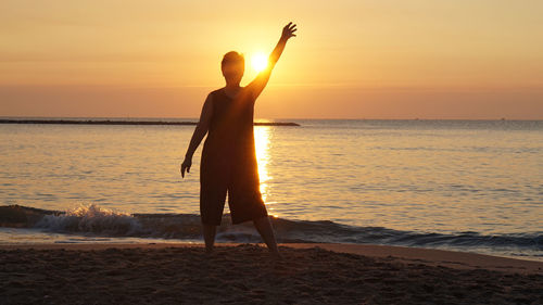 Man standing with arm raised at beach during sunset